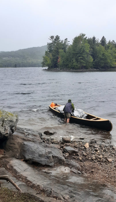 Paddler tends to a canoe along a rocky shore.