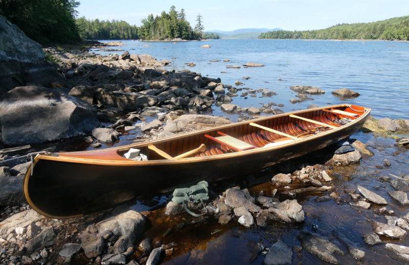 A wooden canoe rests along rocks near a lake.