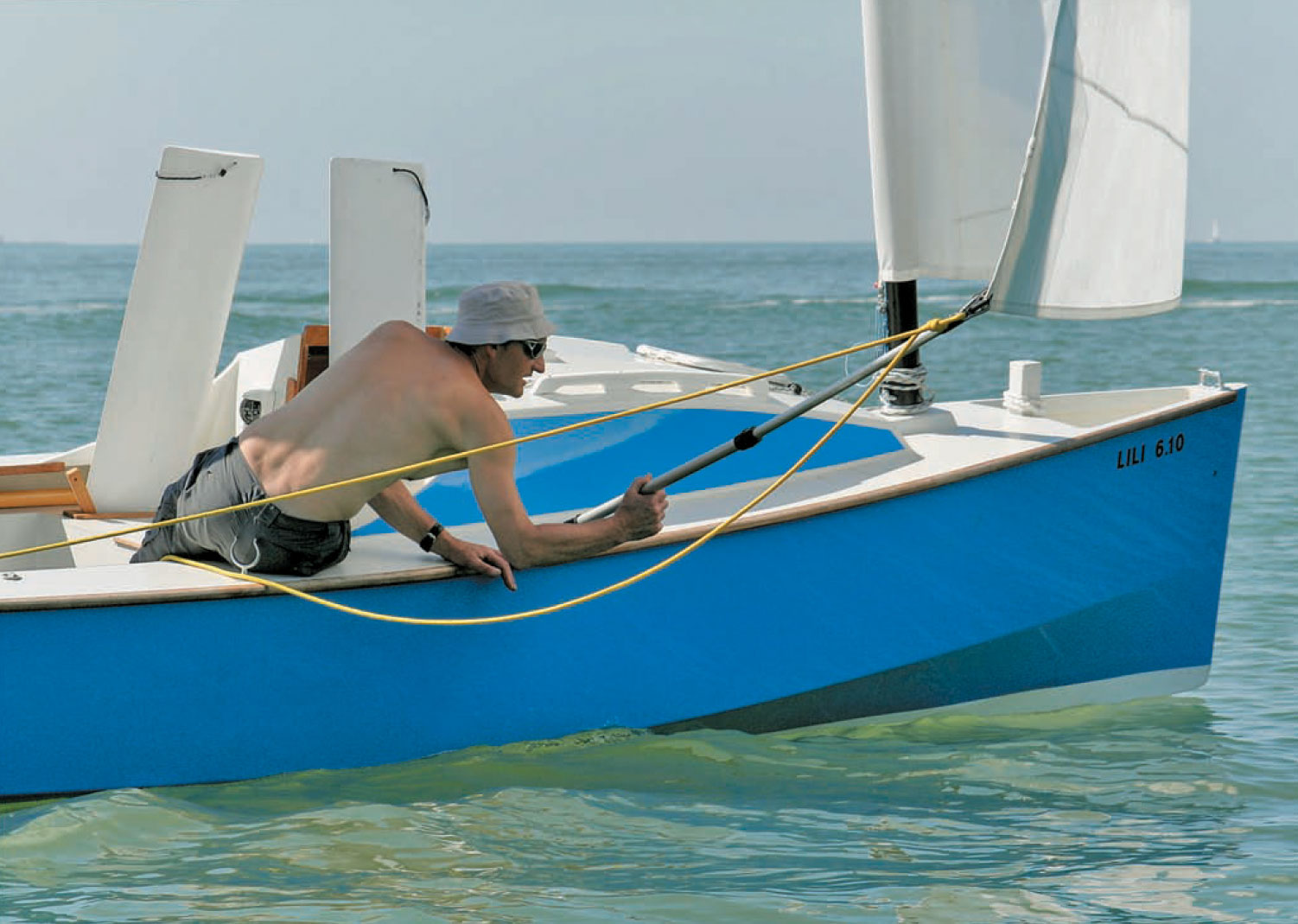 Man adjusts a sail while riding aboard a blue sailboat.
