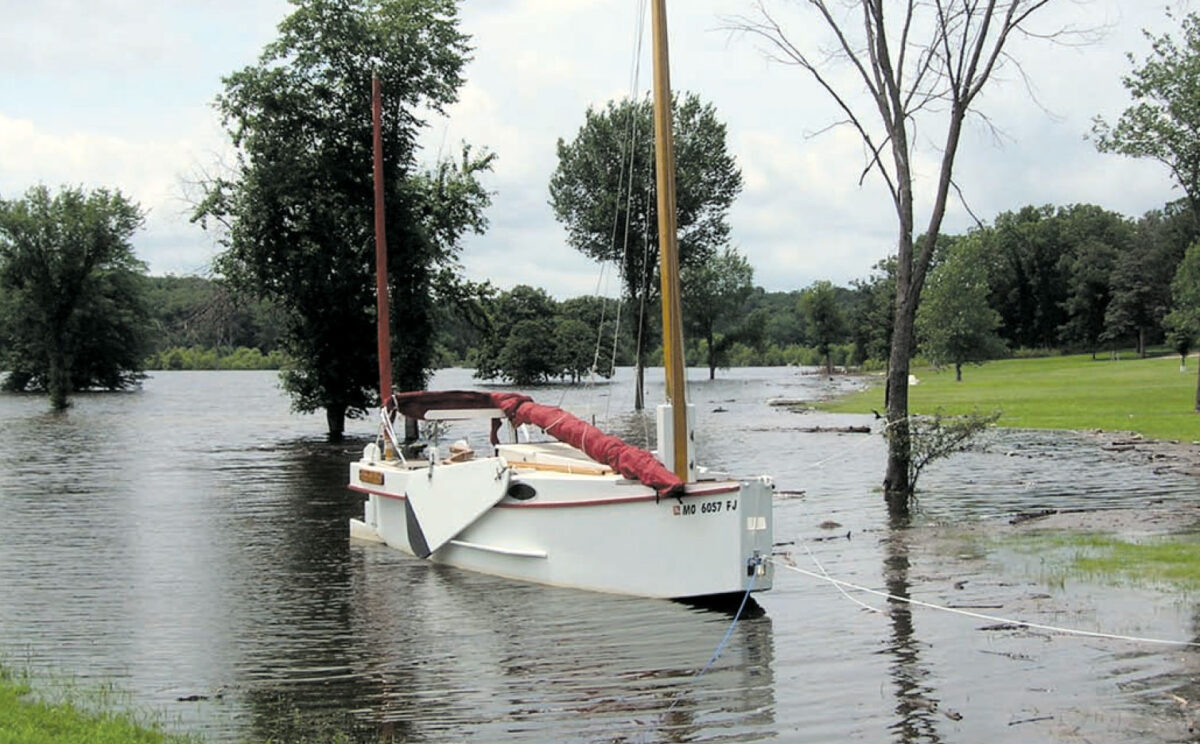 White plywood yawl moored in shallow water with the sails down.