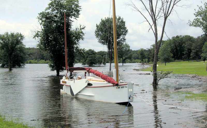 White plywood yawl moored in shallow water with the sails down.