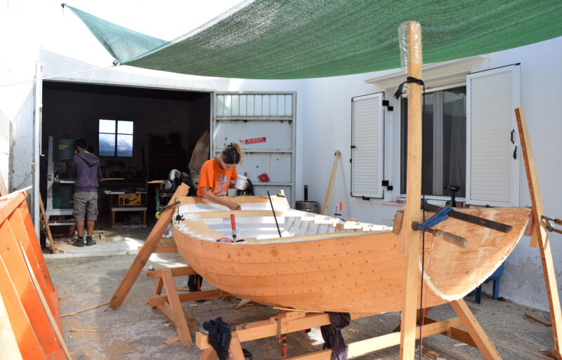 Woman painting the interior of a wooden boat's hull.