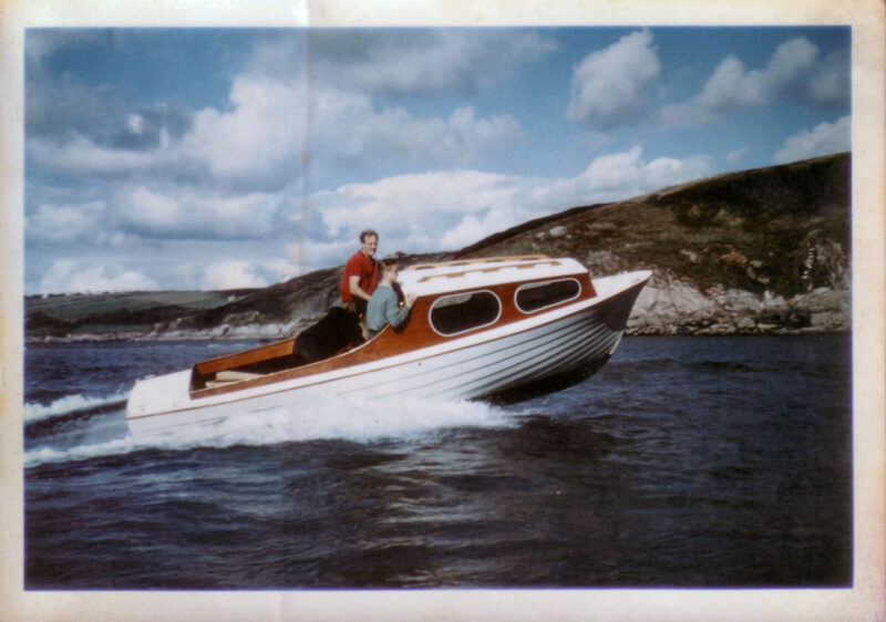 A white-hulled lapstrake 15' speedboat with varnished trim getting up on plane.