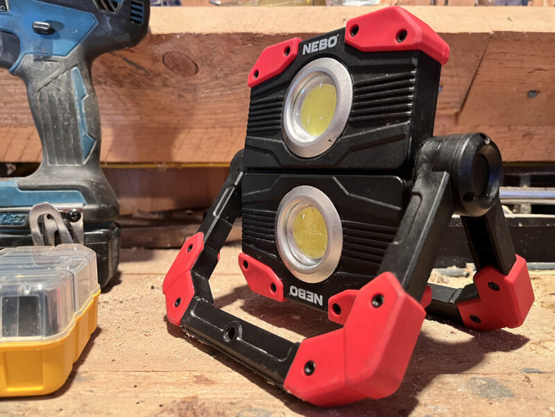 A NEBO Omni 2K work light standing on a wooden work bench.