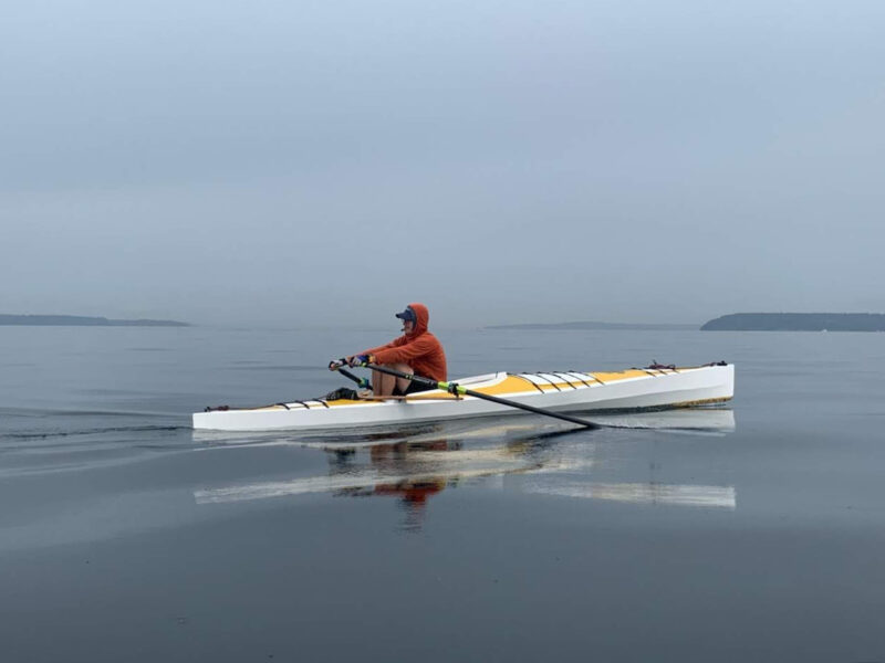 Man rows a white kayak on a cloudy day.